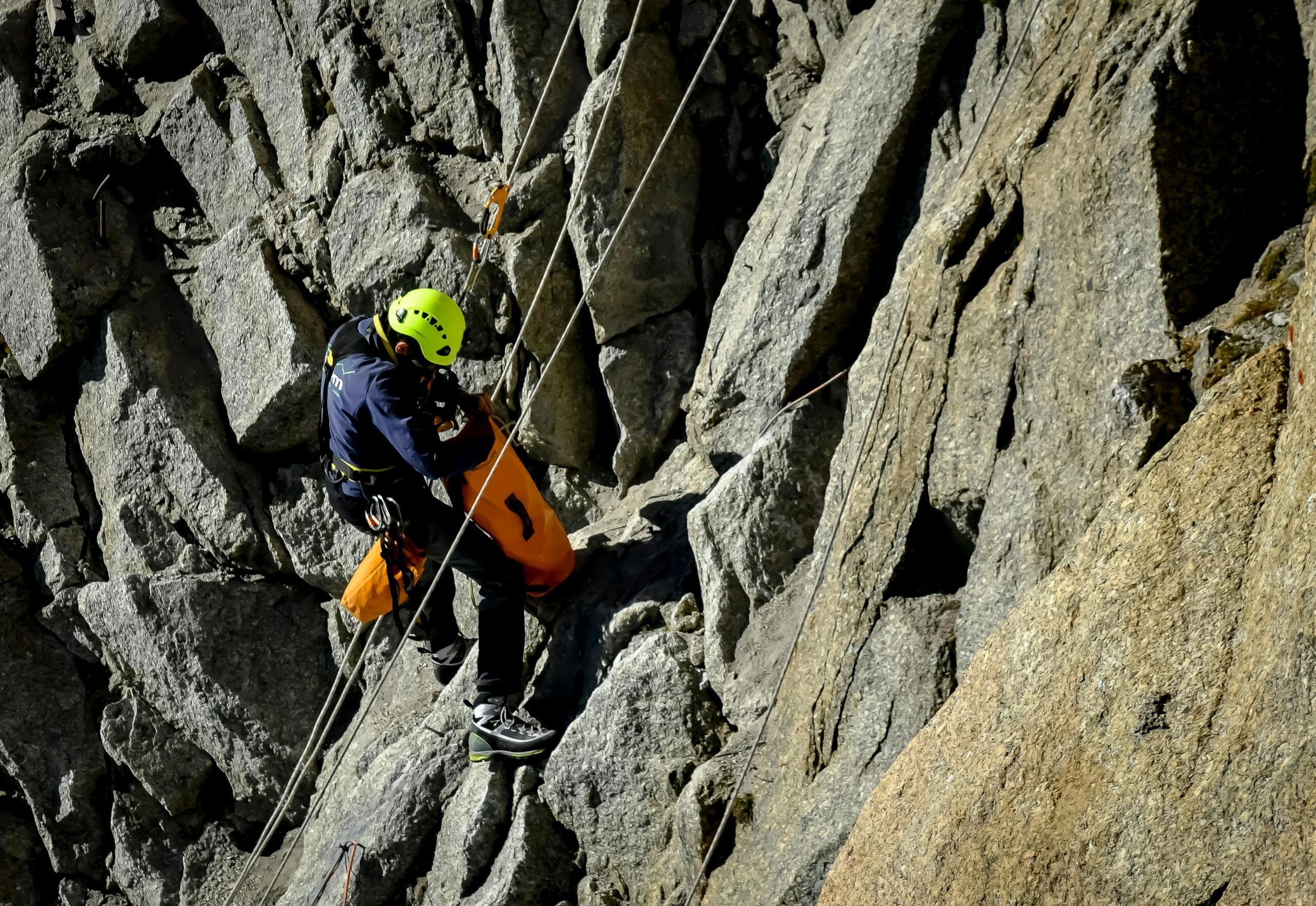 Climber wearing a bright blue helmet while ascending a steep rock face outdoors.