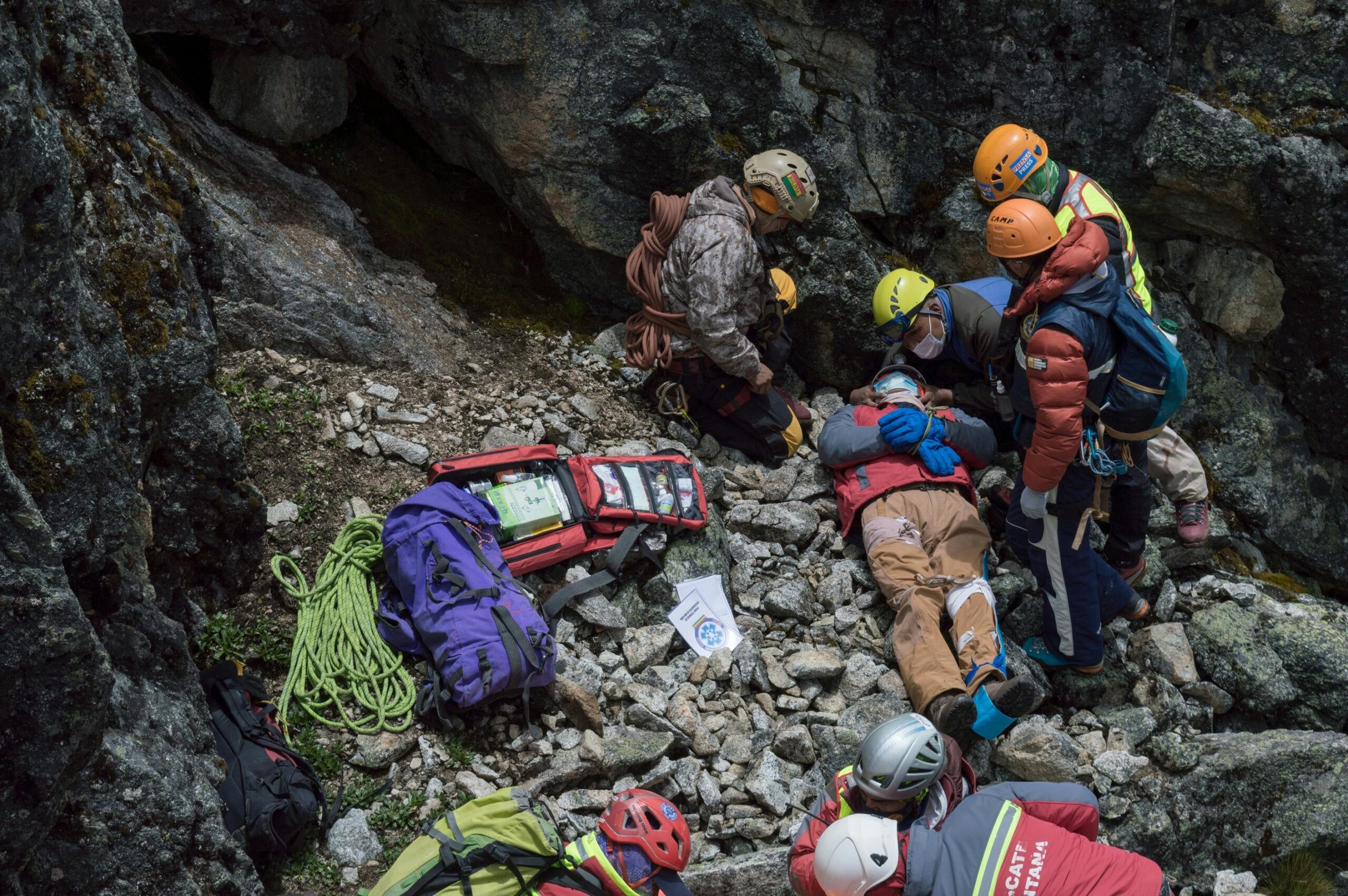Rescued climber being stretchered away with visible helmet protecting her head amidst rocky terrain.